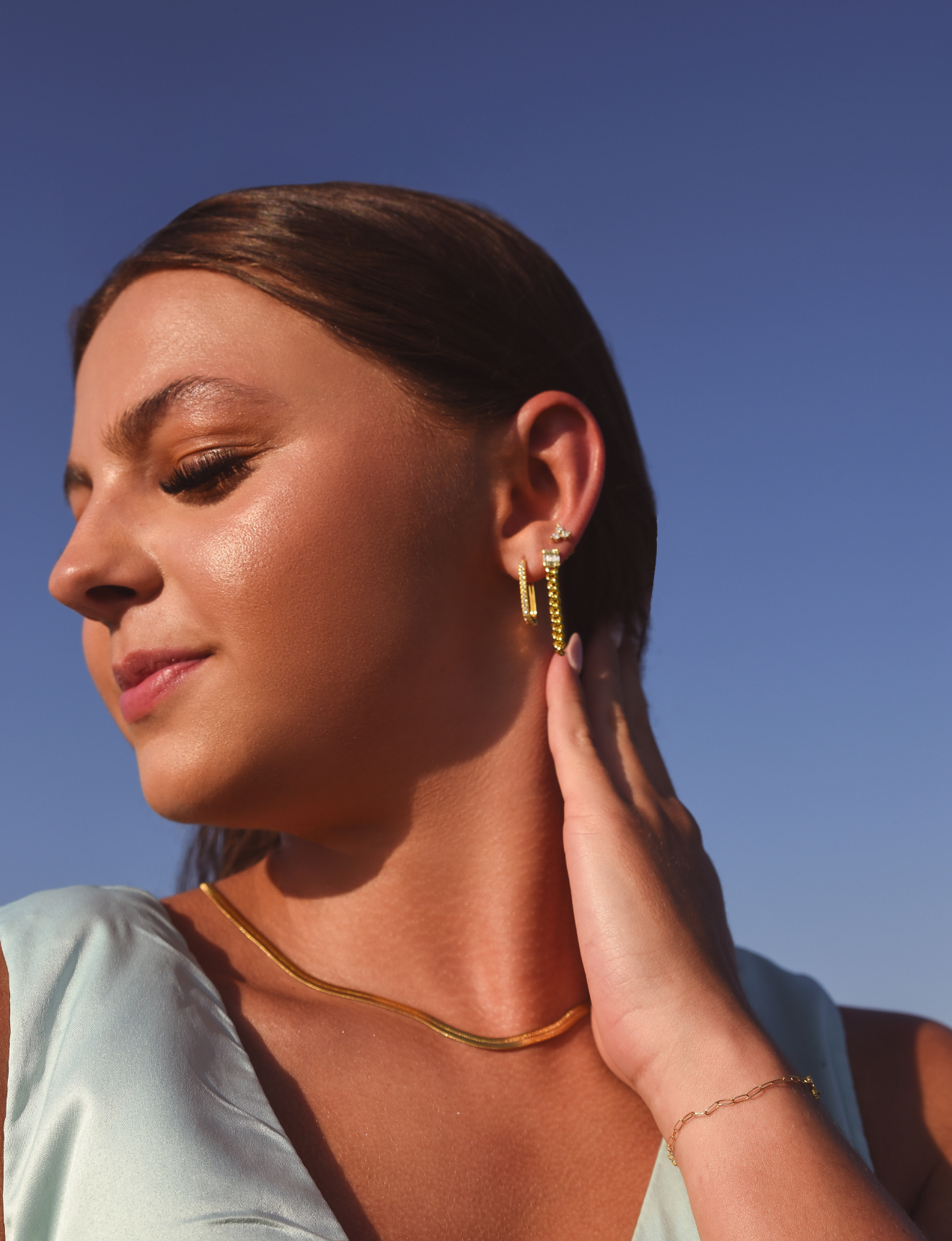 Burdlife Model wearing 3 earrings including the Luxe Oval Hoops, the Refined Single Chain Earring and the Modish Triple Crystal Studs. 