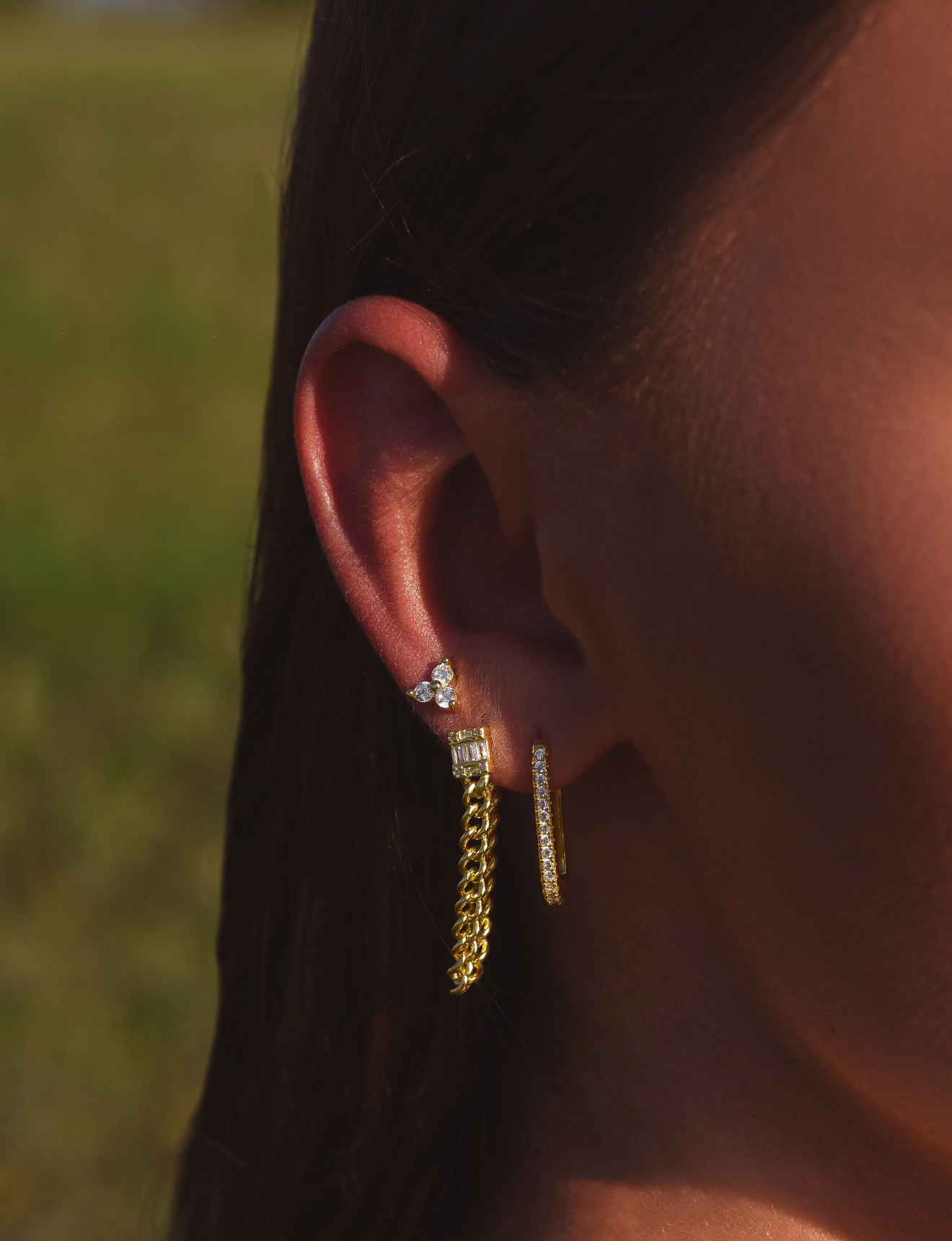 Side of Burdlife Model's head displaying 3 earrings including the Luxe Oval Hoops, the Refined Single Chain Earring and the Modish Triple Crystal Studs. 
